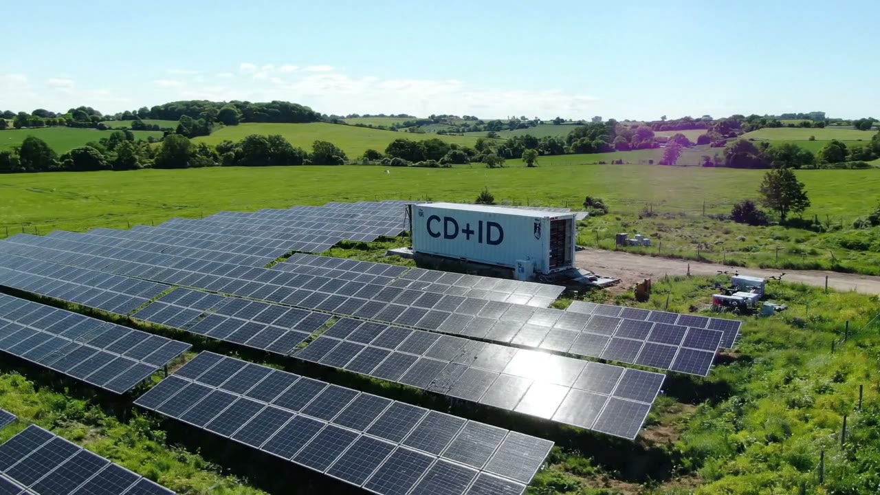 Contenedor rotulado CD+ID junto a un campo de placas solares